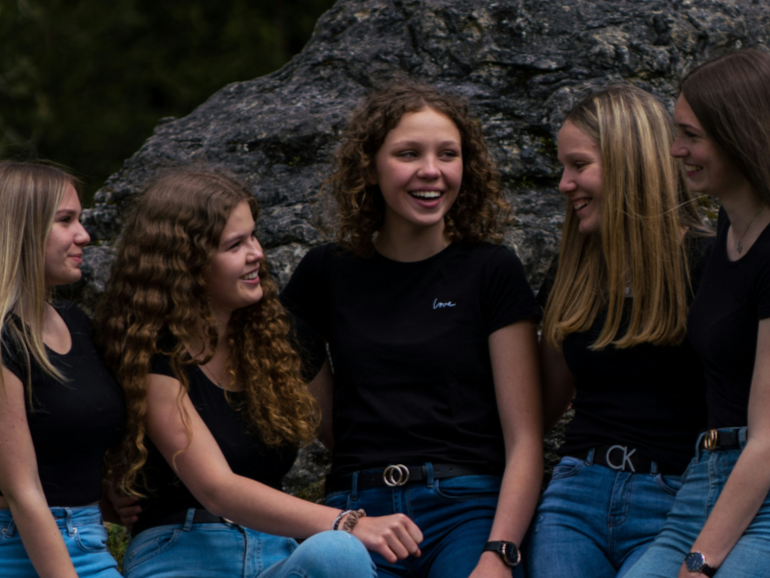 Partage et soutien entre adolescents Boîte à outils : Cinq adolescentes souriantes discutant en groupe, symbolisant l'entraide et les échanges lors des ateliers pour le soutien aux jeunes et parents face à la phobie scolaire.