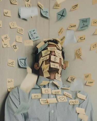 Homme entouré de post-it, semblant accablé par les tâches, illustrant la charge mentale et l’épuisement parental vécus par les familles confrontées au refus scolaire anxieux.